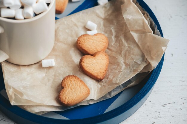 Foto koekjes in de vorm van harten op een blauwe dienblad tegen de achtergrond van koffie met marshmallows valentijnsdag concept