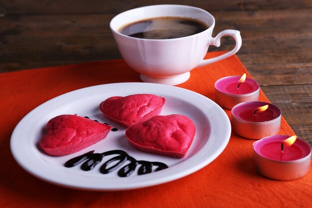 Koekjes in vorm van hart in plaat met kop koffie en kaarsen op servet, op rustieke houten plankenachtergrond