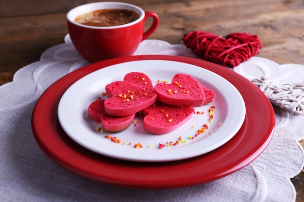 Koekjes in vorm van hart in plaat met kop koffie op servet, op rustieke houten plankenachtergrond