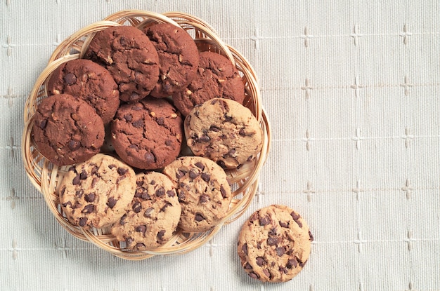 Koekjes met chocolade en noten in rieten plaat op tafelkleed bovenaanzicht