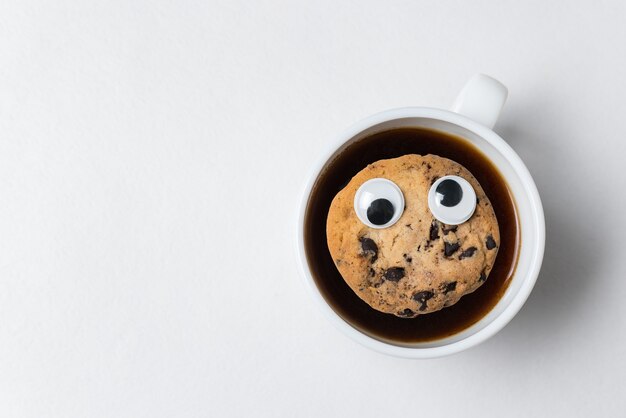 Koekjes met Googly eyes drijvend in kopje thee. Koffiekopje met cookies op witte achtergrond, bovenaanzicht