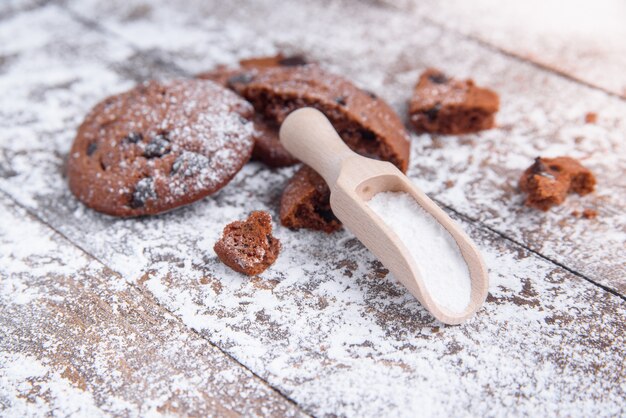 Koekjes met plakjes chocolade bestrooid met poedersuiker en een houten maatlepel. Vers gebak op houten.