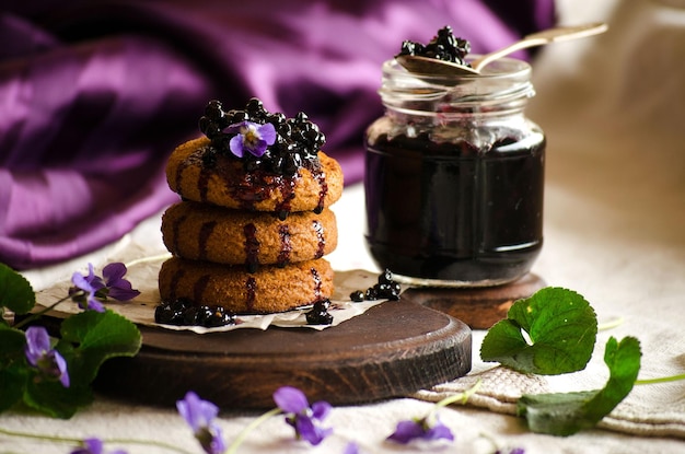 Koekjes met vlierbessenjam en violette bloemen op paarse achtergrond