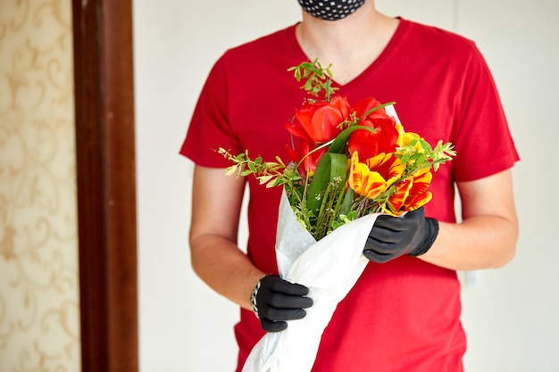 Koerier, bezorger in het rood in medische latexhandschoenen bezorgt online aankopen veilig een boeket bloemen tijdens de coronavirus-epidemie.