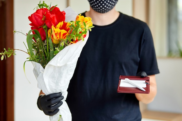 Koerier, bezorger in medische latex handschoenen levert veilig online aankopen van een boeket bloemen