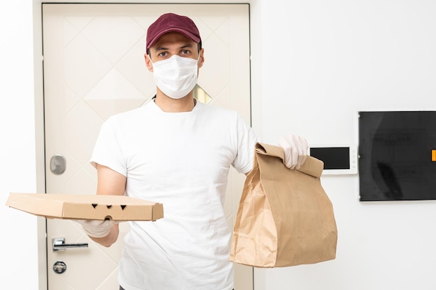 Koerier, bezorger in medische latexhandschoenen en masker levert veilig online aankopen in witte doos aan de deur tijdens de coronavirusepidemie, covid-19. blijf thuis, veilig concept.