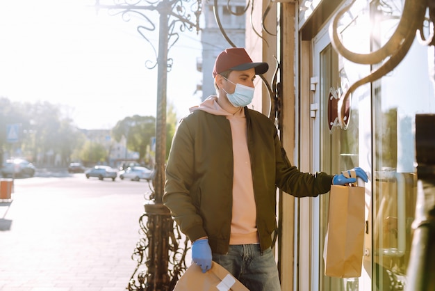 Koerier in beschermend masker en medische handschoenen op een scooter levert ambachtelijke papieren pakket met voedsel. Bezorgservice onder quarantaine, ziekte-uitbraak, coronavirus covid-19 pandemische aandoeningen.