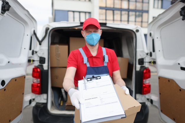 Koerierschauffeur met medisch beschermend masker en handschoenen houdt documenten met ontvangstbewijs voor