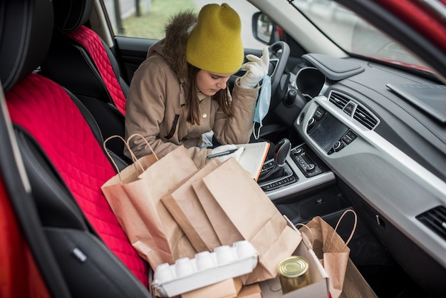 Foto koeriersmeisje in auto. maaltijdbezorgservice. contactloze bezorging, vrijwilliger