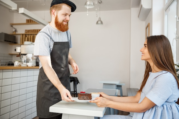 Koffie Business Concept - Kelner of barman die chocoladetaart geeft en met kaukasische mooie dame in blauwe jurk in de koffiewinkel spreekt.