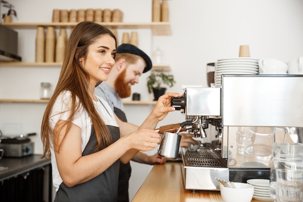 Koffie Business Concept - Portret van dame Barista in schort voorbereiding en stomende melk voor koffie bestellen met haar partner terwijl ze op cafe staan.