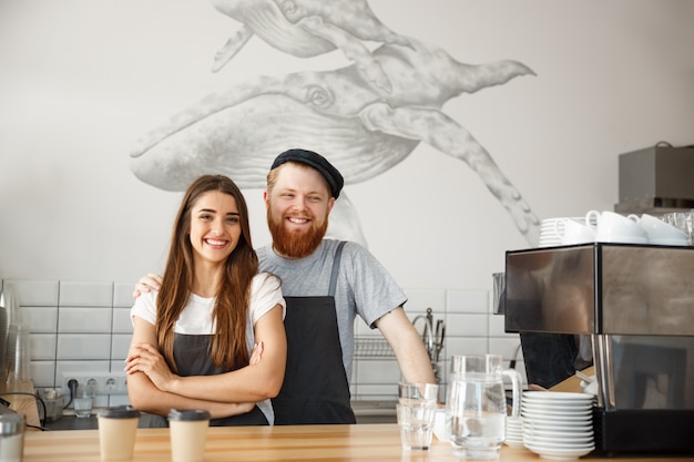 Koffie Business Concept - Positieve jonge bebaarde man en een mooie aantrekkelijke dame barista paar genieten van samenwerken in de moderne koffiewinkel