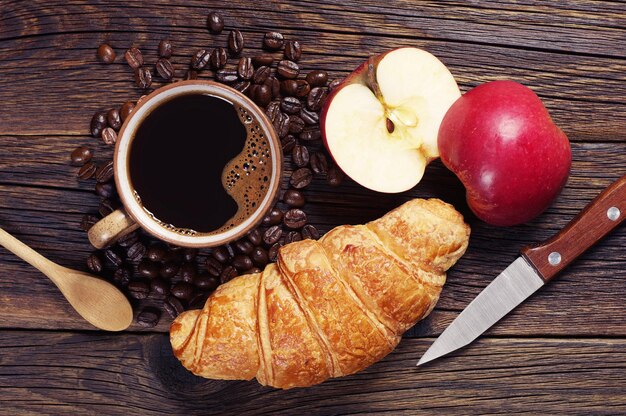 Koffie, croissant en twee helften van een appel op een donkere houten tafel, bovenaanzicht