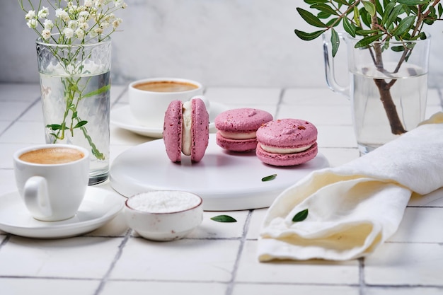 Koffie en macaronstaarten voor het ontbijt voor twee Ochtendtafel met dessertespresso en bloemen in een vaas op een wit betegelde tafel