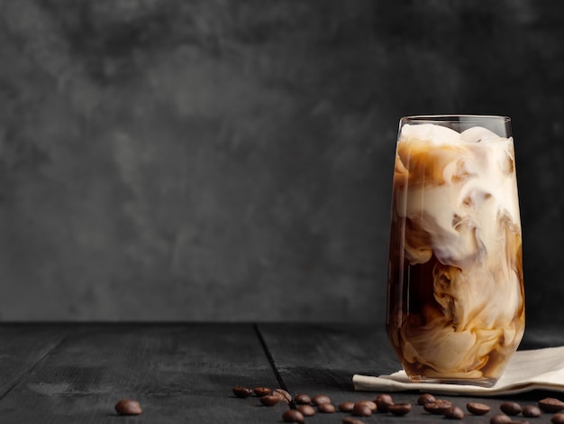 Koffie en melk worden gemengd in een longdrinkglas met ijs. Grijze houten tafel.