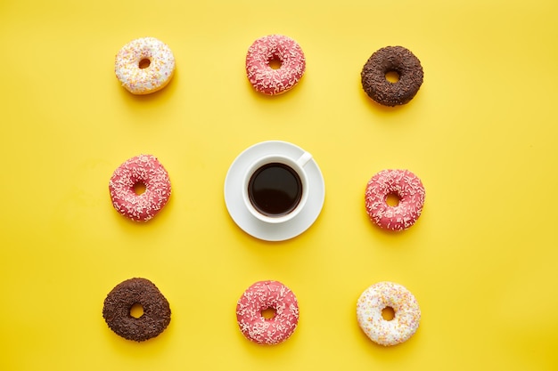 Koffie en zoete donuts op gele achtergrond kopje zwarte koffie in het midden van lekkernijen