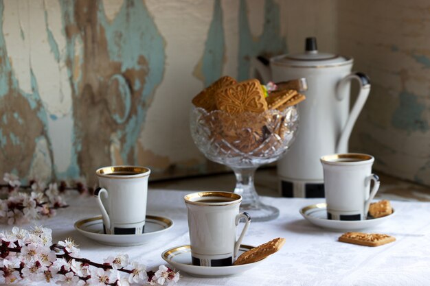 Koffie geserveerd met zandkoekjes en snoep op de achtergrond van bloeiende takken en een oude kast.