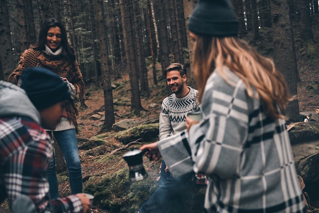 Koffie? Groep gelukkige jonge mensen die samen tijd doorbrengen tijdens het wandelen in het bos