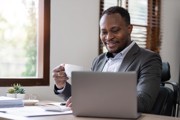 Koffie in de ochtend Portret van een jong bedrijf en succesvol in het vasthouden van een kopje koffie en het werken met een laptop terwijl hij op zijn werkplek zit