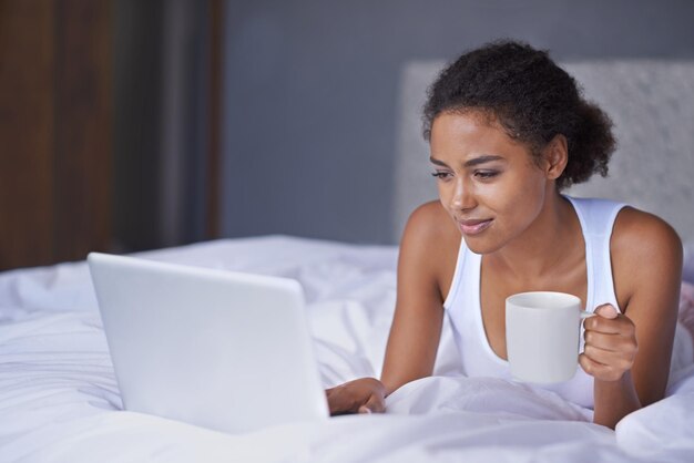 Koffie in de vroege ochtend met een vriend Bijgesneden opname van een jonge vrouw die geniet van een kopje koffie terwijl ze op een laptop werkt