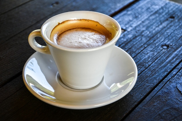 Koffie in witte kop op donkere houten tafel bij coffeeshop. Koffiehuis