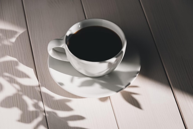 Koffie in witte kop op houten tafel met schaduwen en zonlicht