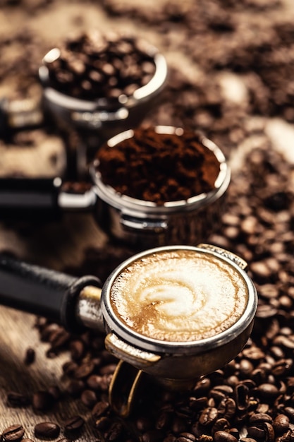 Koffie in zijn verschillende vormen, van rauwe bonen tot gemalen koffie en cappuccino in drie portafilters