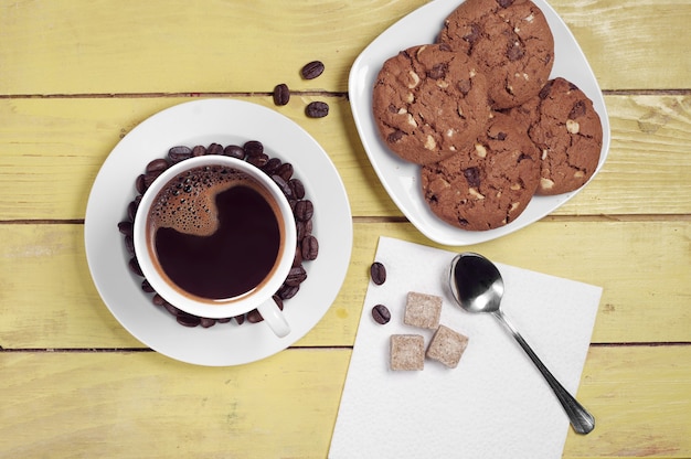 Koffie met chocoladekoekjes op gele houten tafel van bovenaf