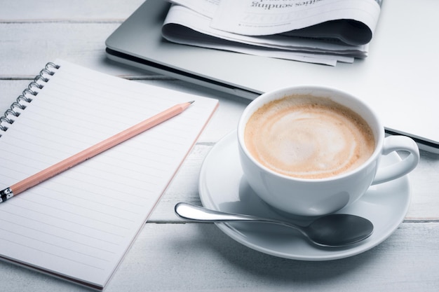 koffie met laptop, krantenpapier, potlood en bril op wit houten tafelblad. Bedrijfsconcept.