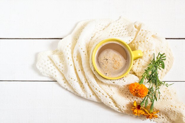 Koffie met melk verpakt in een warme witte gebreide sjaal en bloemen Afrikaantje op witte houten tafel