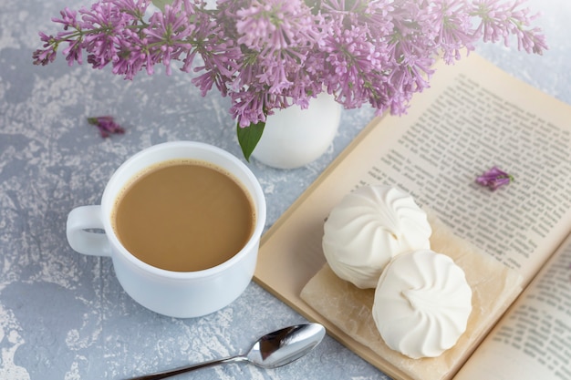 Koffie of thee met melk en marshmallows. Een boek lezen in de tuin met een kopje koffie. Romantisch stilleven met lila bloemen.