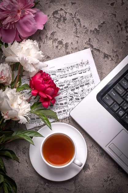 Koffie, pioenrozen en laptop op grijze vintage background