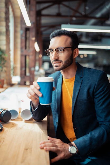 Koffie voor het werk. Donkerharige knappe interieurontwerper die koffie drinkt voordat hij aan het werk gaat