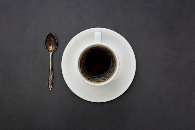 Koffie. Witte kop van koffie bovenaanzicht lepel en plaat op donkere achtergrond