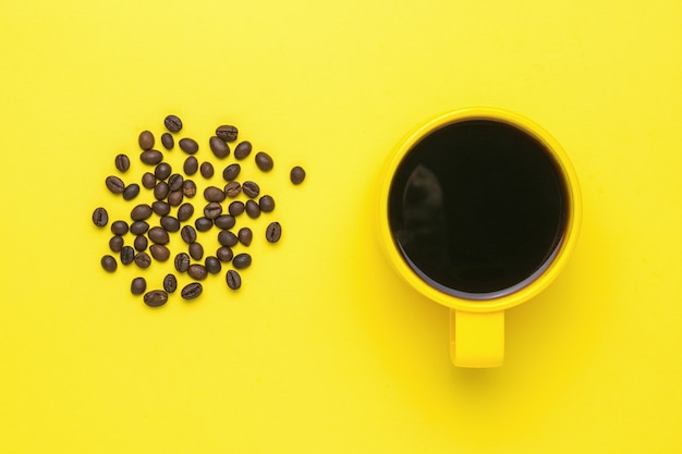 Koffiebonen en een gele kop met een drankje op een gele achtergrond. Een populaire warme drank en apparatuur voor creativiteit.