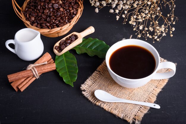 Koffiebonen en koffieblad met melk op zwarte houten tafel