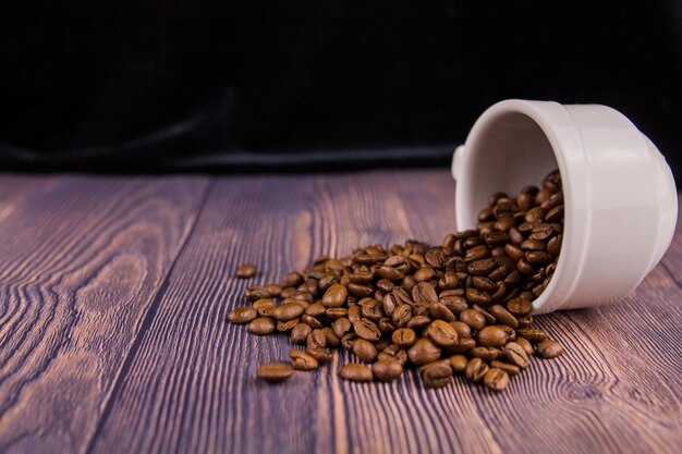 Koffiebonen gestrooid uit een witte kop op een houten tafel