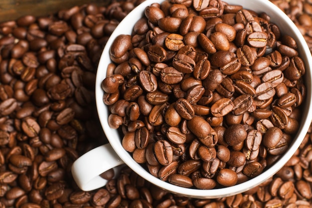 Koffiebonen in een witte kop en op een hoop koffiebonen