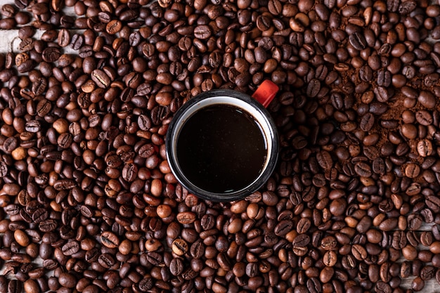 Koffiebonen met een rode metalen beker in het midden met vers gemaakte koffie