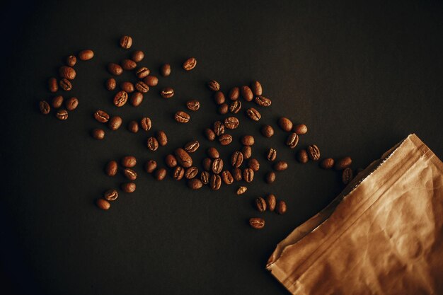 Koffiebonen verspreid van papieren pak op zwarte achtergrond Plat leggen Verse aromatische gebrande koffiebonen bovenaanzicht Coffeeshop concept Donker humeurig beeld