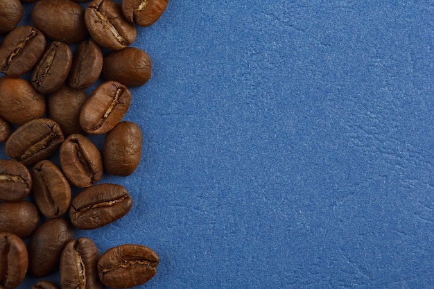 Koffiebonen zijn verspreid op een blauwe achtergrond vanaf de rand van het frame Koffie op een blauwe