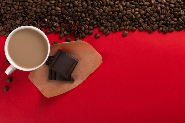 Koffiebonen zijn verspreid op een rood papier en een witte kop, chocolade, commerciële copyspace.