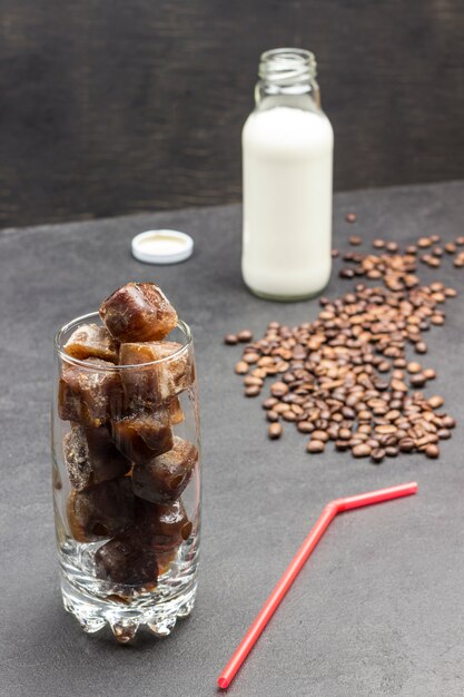 Koffieijsblokjes in glas. Glas met melk. Korrels van koffie en rood stro