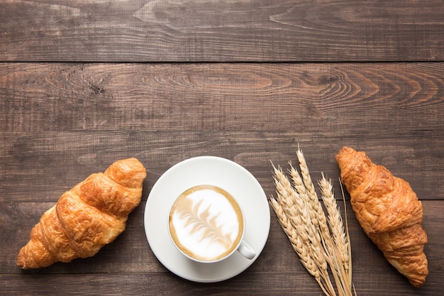 Koffiekop en verse gebakken croissants op houten achtergrond. Bovenaanzicht