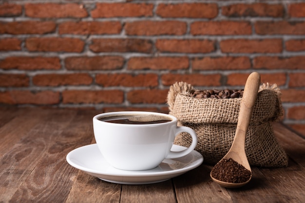 Koffiekop, koffiedik en koffiebonen in jute op houten lijst met bakstenen muur