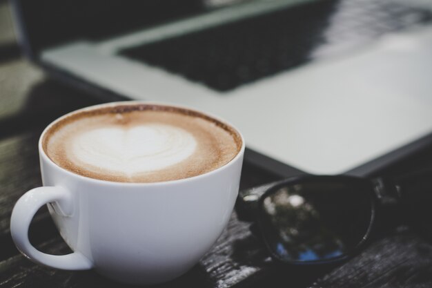 Koffiekop met de bovenkant van het computerlaboratorium die aan de houten lijst werken.