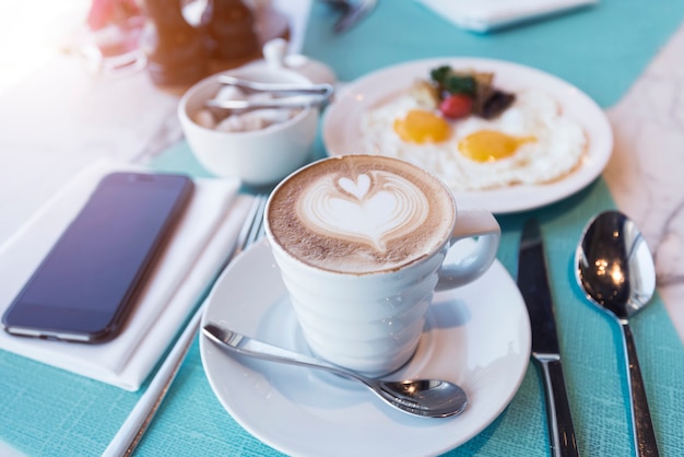 Koffiekop met mobiel op tafel met ontbijt. vrije tijd. zakelijke verbindingstechnologie.