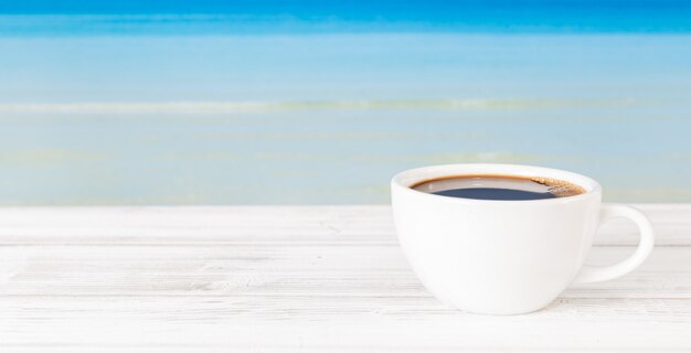 Koffiekop op witte houten lijst met heldere blauwe overzeese achtergrond