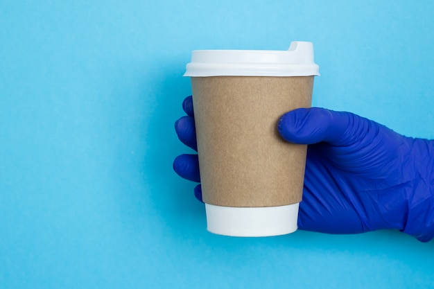 Koffiekop ter beschikking geïsoleerd op blauwe achtergrond. Hand met papieren beker.