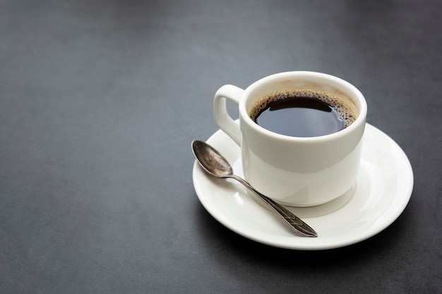 Koffiekopje geïsoleerd. Witte kop van koffie bovenaanzicht lepel en plaat op donkere achtergrond